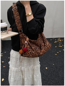 Detail of leopard print tote bag with wide strap and fuzzy pompom charm in autumn street setting