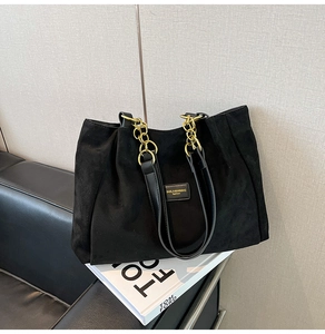 Detail of black matte suede tote bag featuring gold chain strap and metal logo plaque