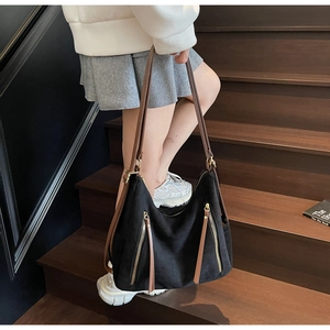 Detail of black frosted tote bag with metal zippers and brown leather straps