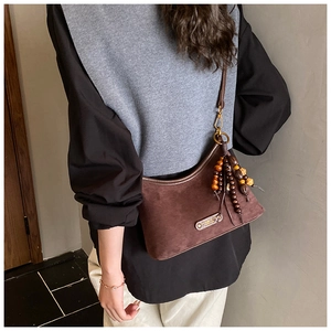 Close-up of vintage brown suede crossbody bag with ethnic wooden bead charm and metal tag