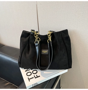 Detail of black suede tote bag featuring a leather and gold chain handle on books