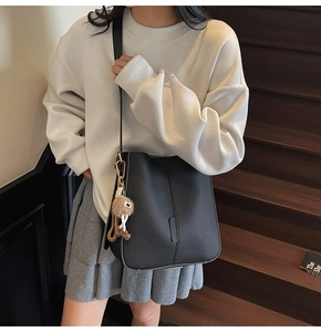 Détail du sac seau noir en cuir grainé avec pendentif en peluche et bandoulière fine
