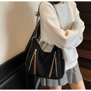 Detail of a black textured tote bag with vertical zippers and brown leather zipper pulls