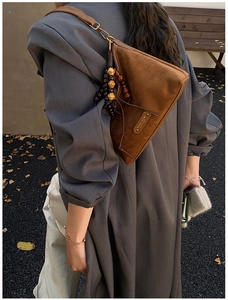 Close-up of brown suede dumpling bag with dark brown beaded charm and metal logo tag