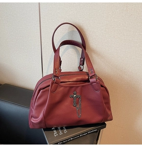 Detail of dark wine red lychee texture handbag featuring a gothic cross and chain ornament