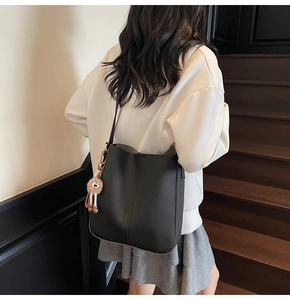 Détail du sac seau noir en cuir grainé avec un charme en peluche et coutures verticales