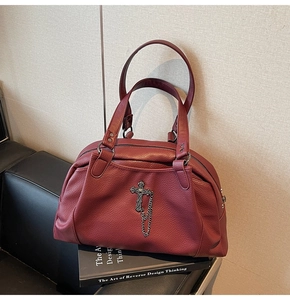 Close-up of wine red textured leather handbag with silver cross pendant and metal chains