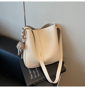 Détail du sac seau beige avec texture litchi, bandoulière large et pompon en fourrure