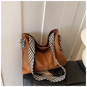Detail of a brown matte tote bag with black and white striped woven wide shoulder strap