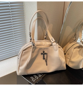 Detail of off-white textured leather handbag with vintage metal cross and chain decor