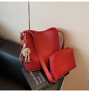 Détail du sac seau rouge grainé avec pochette et breloque chouette sur des livres