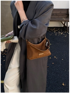 Détail d'un sac bandoulière en daim marron avec logo métallique et finitions dorées