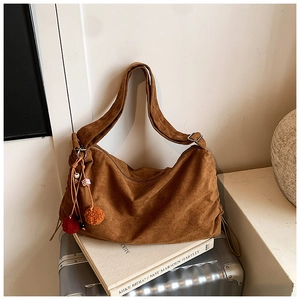 Brown suede hobo bag with colorful tassel charms on a vintage suitcase setting