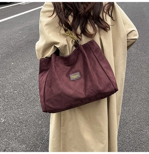 Close-up of burgundy suede tote bag featuring a chunky gold chain strap and leather logo tag