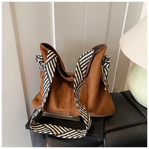 Detail of a brown suede tote bag featuring a black and white woven knot shoulder strap
