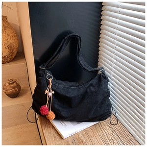 Detail of black corduroy hobo bag with colorful pompom charm on a wooden surface