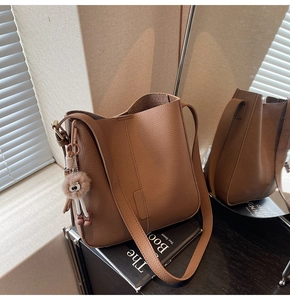 Gros plan du sac seau en cuir marron à motif litchi avec un joli pompon décoratif