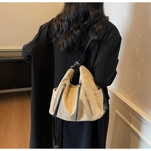Close-up of beige suede hobo bag with vertical zippers and black straps on a model