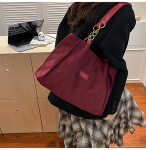 Close-up of burgundy suede tote bag featuring gold chain strap and branding detail