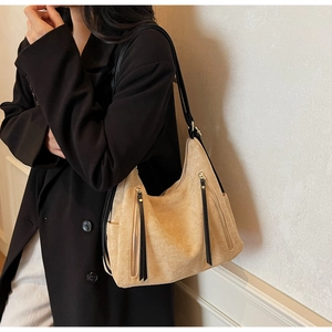 Detail of beige suede shoulder bag featuring long black leather tassel and side zipper pocket
