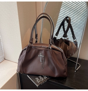 Close-up of brown pebbled leather Boston bag with metal cross chain on black surface
