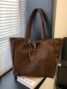 Leopard print suede tote bag with front pocket and Own The Moment tag in warm indoor lighting
