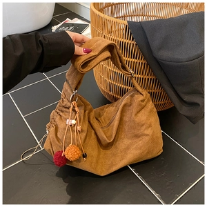 Detail of a brown suede half-moon tote bag with colorful pompom charms and wooden beads