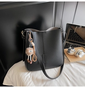 Détail d'un sac seau en cuir noir grainé avec breloque peluche sur un bureau en bois
