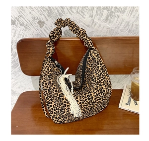 Detail of leopard print tote bag featuring ruffled handles and pearl lace charms on a bench