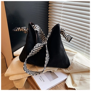 Detail of black suede tote bag featuring a striped woven strap and knot decoration