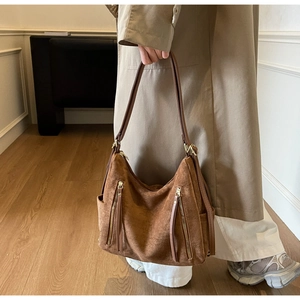 Detail of a large brown suede tote bag with zipper pockets worn with a beige trench coat