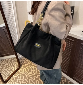 Detail of black large tote bag featuring metal chain shoulder strap and logo patch