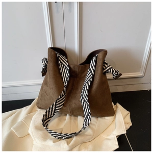 Close-up of brown suede shoulder bag with striped fabric strap and decorative knot detail