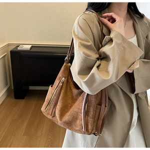 Detail of vintage brown suede tote bag with dual metal zippers on a khaki trench coat