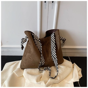 Detail of a large brown matte tote bag with a striped woven strap and side knot accents