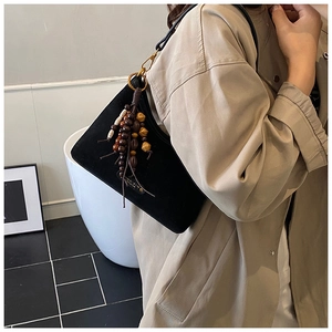 Detail of black suede shoulder bag featuring decorative wooden bead tassel and metal plate