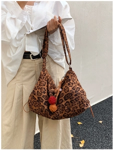 Close-up of leopard print tote bag with red and orange pom-pom charms in autumn setting