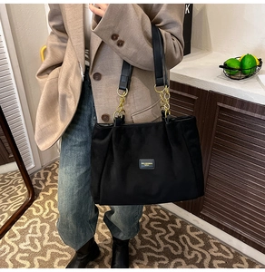 Detail of black tote bag with gold chain strap and brand label on a casual beige blazer