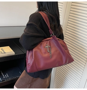 Detail of burgundy gothic tote bag with silver cross charm and chain on shoulder