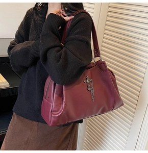 Close-up of burgundy leather tote bag with silver cross pendant and tassel detail