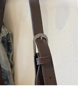Detail eines dunkelbraunen Lederriemens mit Metallschnalle und feinen Nähten an der Tasche
