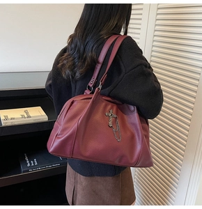 Detail of burgundy pebbled leather tote bag with metal cross pendant and chain decoration