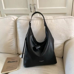 Dettaglio di borsa hobo in pelle nera minimalista con logo su un divano beige