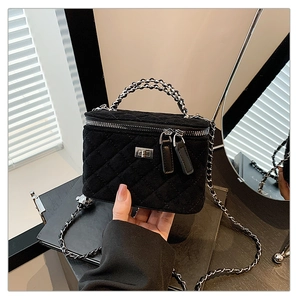 Detail of a black quilted vanity bag featuring a silver twist lock and chain strap