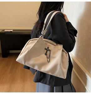Detail of beige pebble leather tote bag featuring vintage metal cross charm and chain