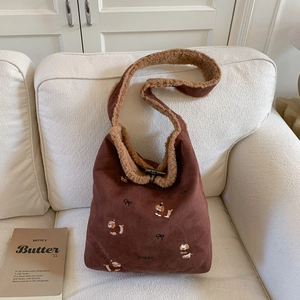 Detail of plush brown tote bag featuring puppy embroidery and sherpa trim on white sofa