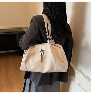 Detail of a beige textured leather tote with vintage metal cross pendant and chain fringe