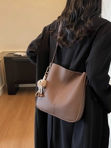 Sac seau marron en cuir grainé avec pendentif en peluche porté par un mannequin