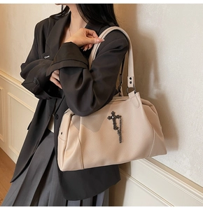 Detail of cream lychee leather tote bag with metallic cross and chain tassel charm
