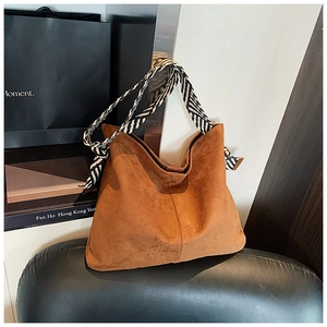 Detail of a brown suede hobo bag featuring a knotted black and white striped woven strap